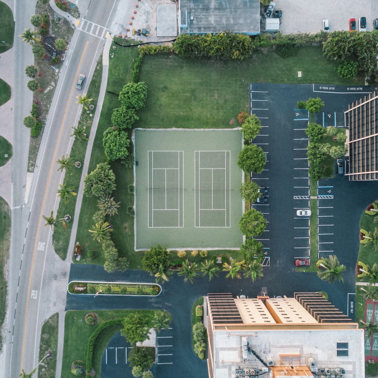 Overhead aerial view of a commercial property showing marked parking bays, tennis courts, a roadway and landscaped boundaries